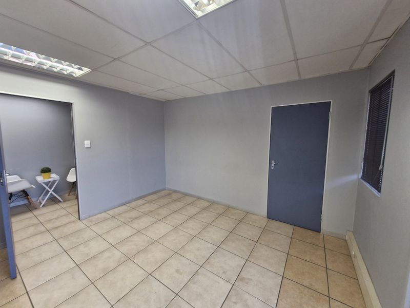 A vacant office space featuring neutral grey walls, ceramic tiled flooring, and a suspended ceiling with integrated lighting.
