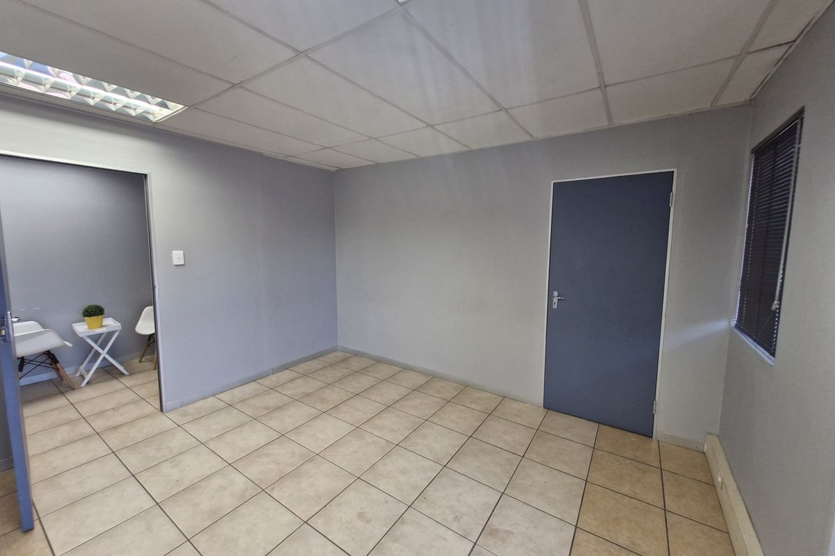 A vacant office space featuring neutral grey walls, ceramic tiled flooring, and a suspended ceiling with integrated lighting.