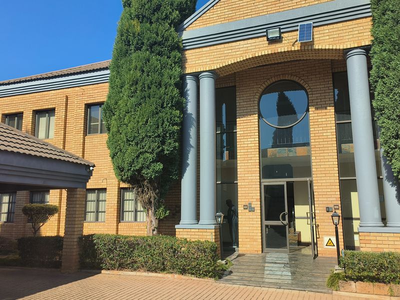 A professional office building exterior featuring a brick facade, prominent columns, a circular window, and a paved entrance area with mature landscaping.