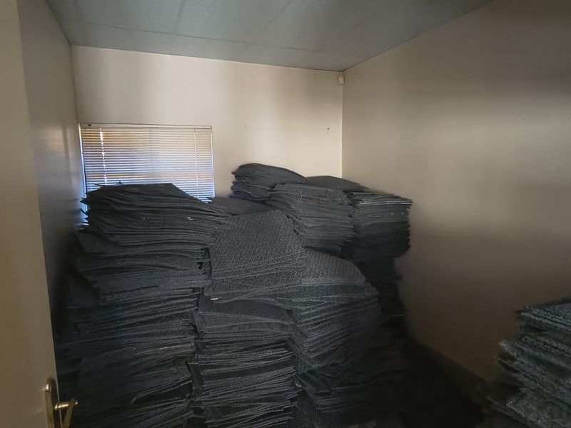 A small utility or storage room featuring a suspended ceiling and a window with venetian blinds, currently used for bulk storage.