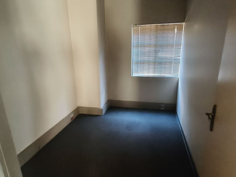 A compact, empty office space featuring neutral walls, carpeted flooring, and a window fitted with horizontal blinds.