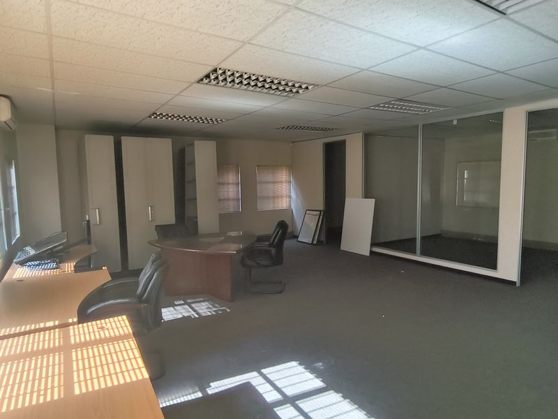 A spacious office area featuring carpeted flooring, a suspended ceiling with recessed lighting, and a glass-partitioned private office space.