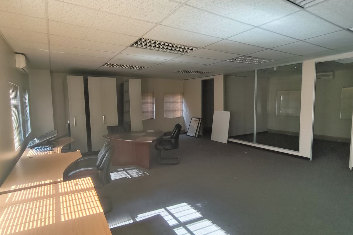 A spacious office area featuring carpeted flooring, a suspended ceiling with recessed lighting, and a glass-partitioned private office space.