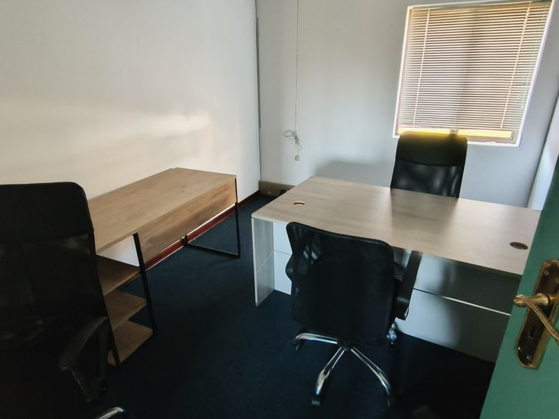 A functional office space featuring carpeted flooring, neutral walls, and a window with fitted blinds, providing a practical work environment.