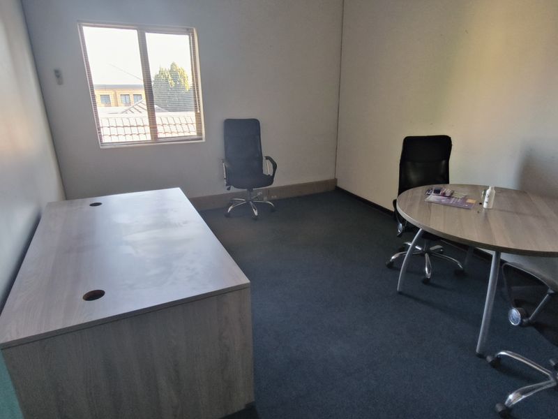 A functional office space featuring carpeted flooring and a window with blinds, providing a practical environment for professional work.
