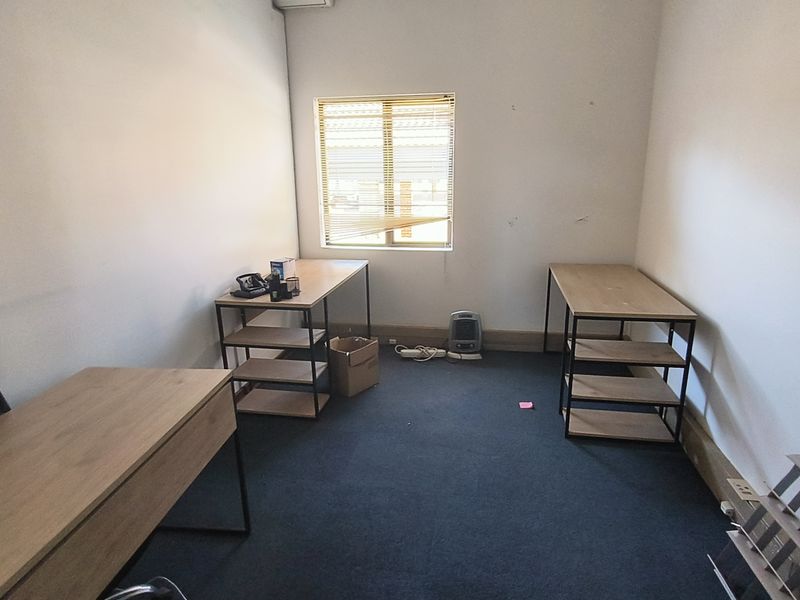 A functional office space featuring carpeted flooring and a window with integrated blinds, suitable for a professional work environment.