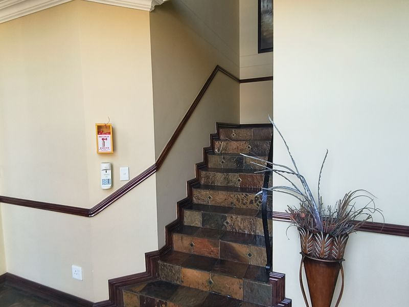 A well-maintained office hallway featuring a stone-tiled staircase with a wooden handrail and clear directional signage.