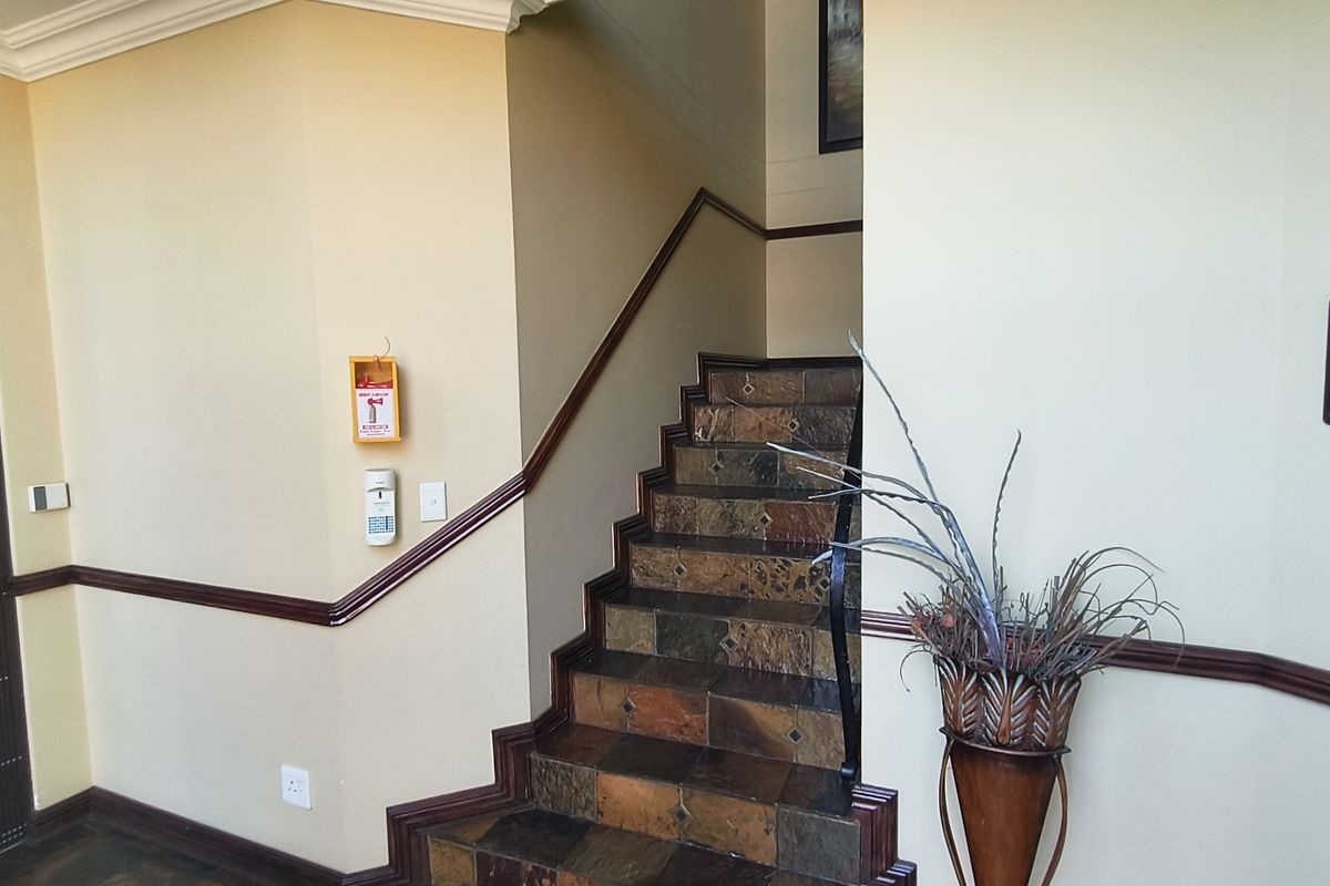A well-maintained office hallway featuring a stone-tiled staircase with a wooden handrail and clear directional signage.