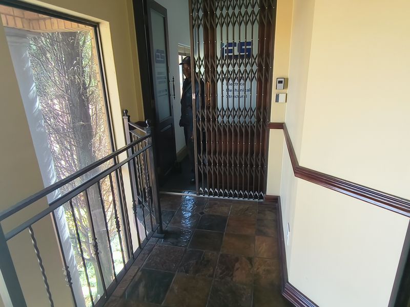 A secure office entrance featuring tiled flooring, wrought iron railings, and a protective security gate at the doorway.
