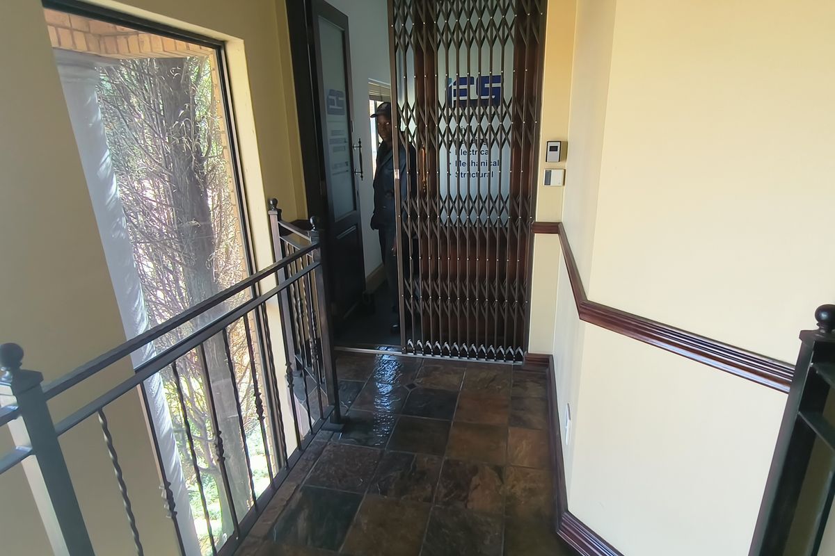 A secure office entrance featuring tiled flooring, wrought iron railings, and a protective security gate at the doorway.
