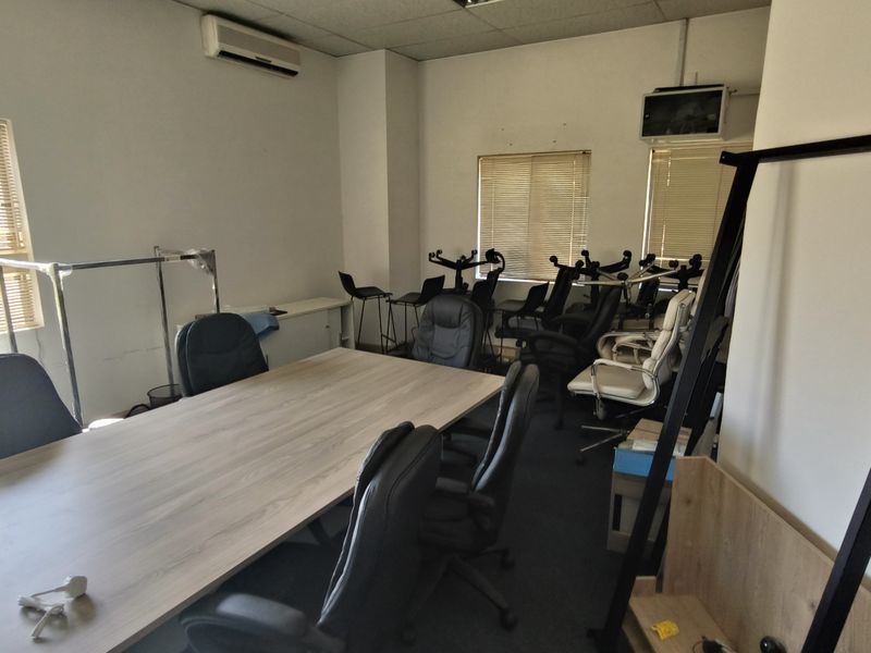 A functional office space featuring carpeted flooring, a suspended ceiling, venetian blinds, and a wall-mounted split-system air conditioning unit.