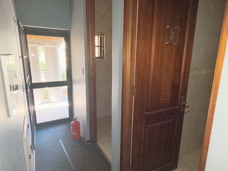 A functional office hallway featuring tiled flooring, a timber door, and a security gate leading to an outdoor area.