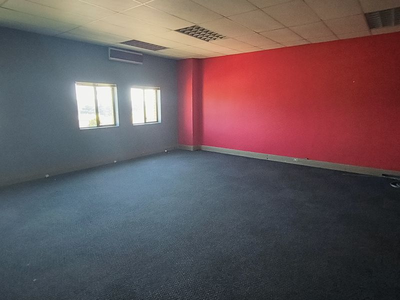 A spacious, empty office area featuring a suspended ceiling, recessed lighting, air conditioning, and carpeted flooring with a bold red accent wall.