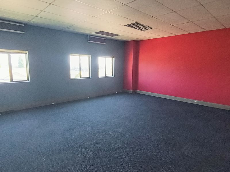 An empty office space featuring a suspended ceiling, recessed lighting, air conditioning units, and carpet flooring with contrasting grey and red painted walls.