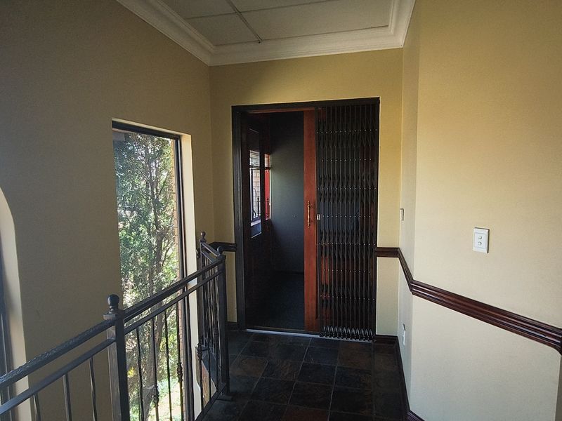 A hallway featuring slate tile flooring, a wrought iron balustrade, and a security gate leading to an adjacent room.