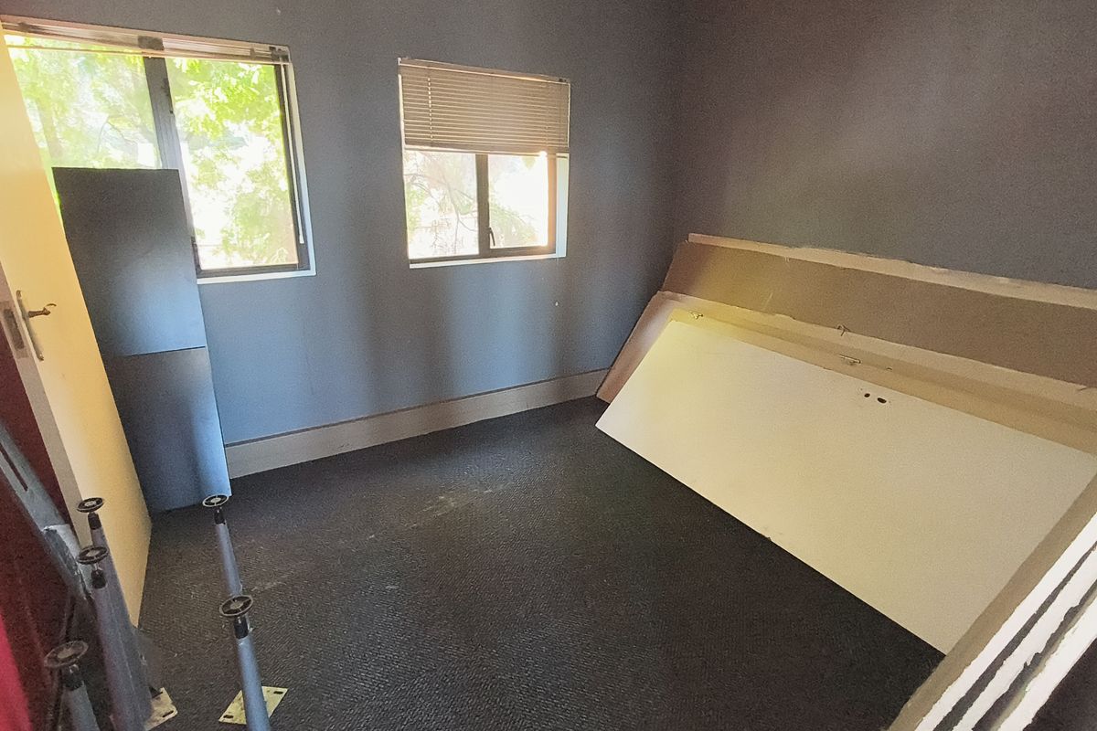 A vacant office space featuring carpeted flooring, dual windows with venetian blinds, and grey painted walls, currently undergoing minor maintenance or renovation.