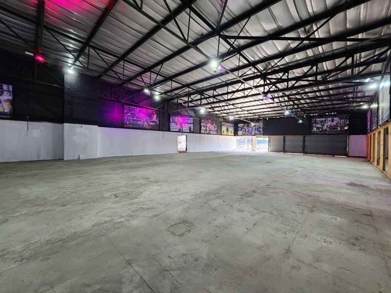 Large open-plan industrial retail space featuring high exposed steel roof trusses, concrete flooring, and multiple roller shutter doors.