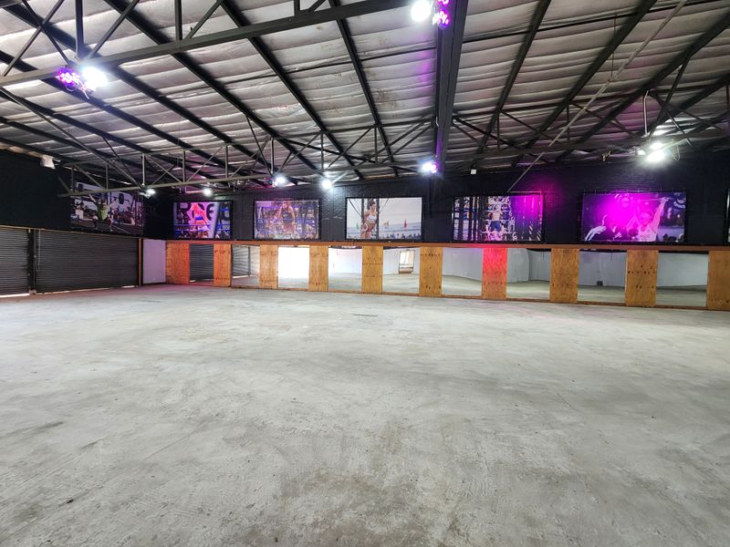 Spacious open-plan gym area featuring high exposed ceilings, industrial lighting, and a full-length mirrored wall, suitable for various fitness or commercial uses.
