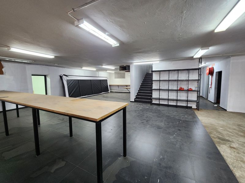 A spacious, open-plan utility or storage area featuring tiled flooring, industrial lighting, a staircase, and built-in metal shelving.