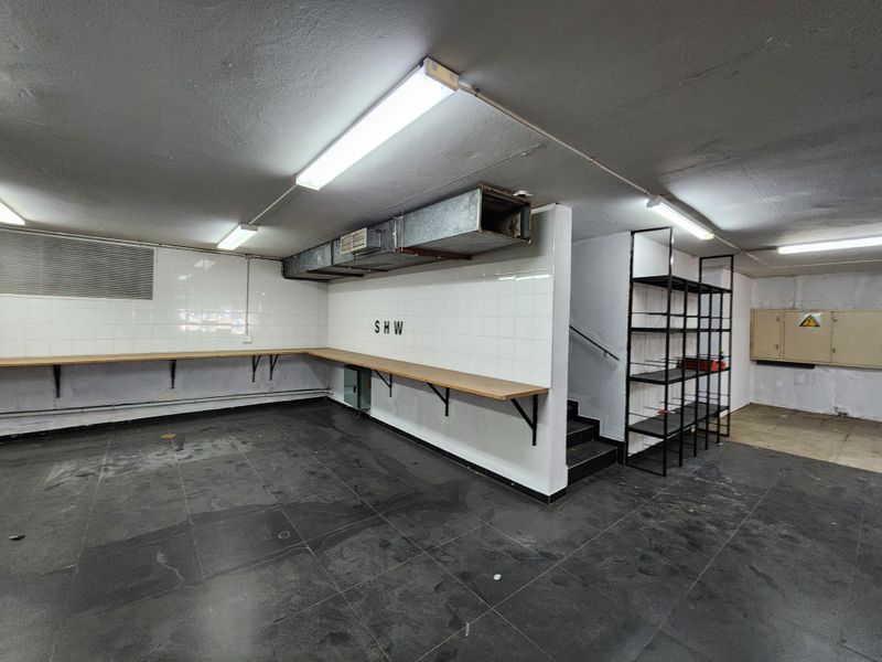 A functional utility or storage space featuring tiled walls, a fixed timber workbench, exposed HVAC ducting, and direct access to a staircase.