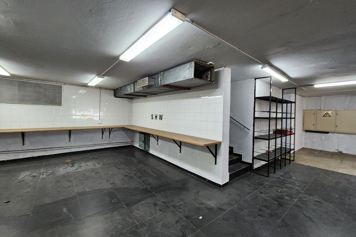 A functional utility or storage space featuring tiled walls, a fixed timber workbench, exposed HVAC ducting, and direct access to a staircase.