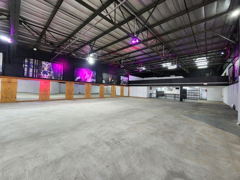 Spacious open-plan gym area featuring high exposed steel ceilings, a full-length mirrored wall, and durable concrete flooring, suitable for various fitness activities.