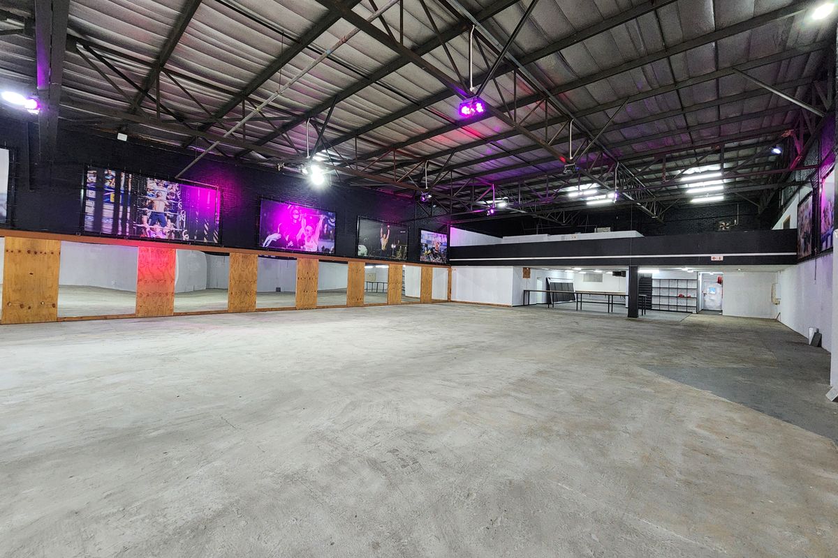Spacious open-plan gym area featuring high exposed steel ceilings, a full-length mirrored wall, and durable concrete flooring, suitable for various fitness activities.