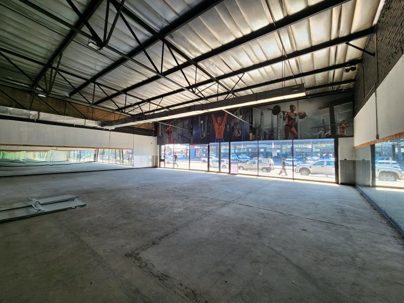 Spacious open-plan retail or commercial unit featuring high industrial ceilings, large glass storefront windows, and full-length wall mirrors.