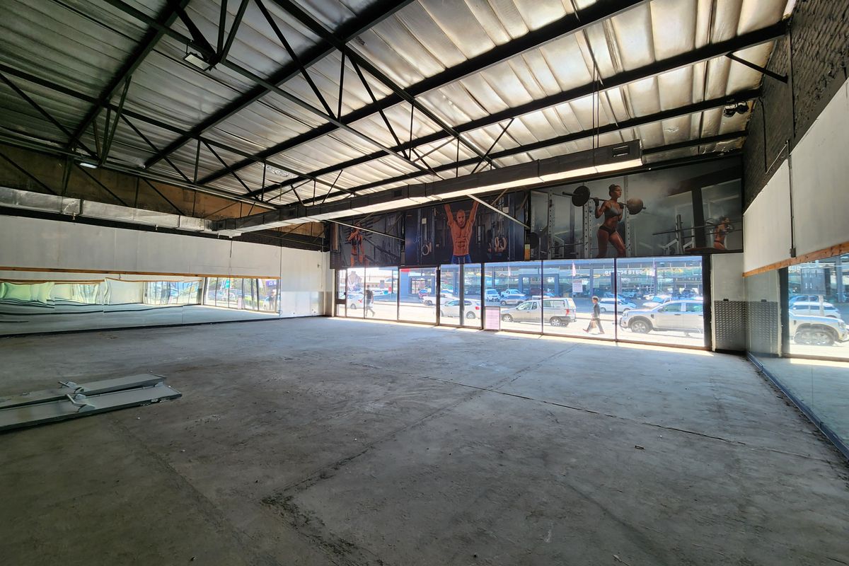 Spacious open-plan retail or commercial unit featuring high industrial ceilings, large glass storefront windows, and full-length wall mirrors.