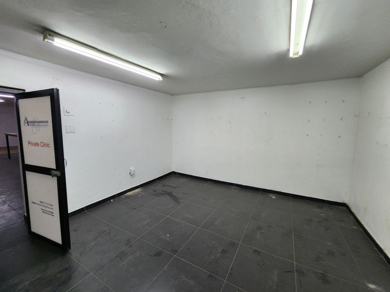 An empty, utilitarian room featuring dark tiled flooring, white walls, and overhead fluorescent lighting, suitable for office or storage use.