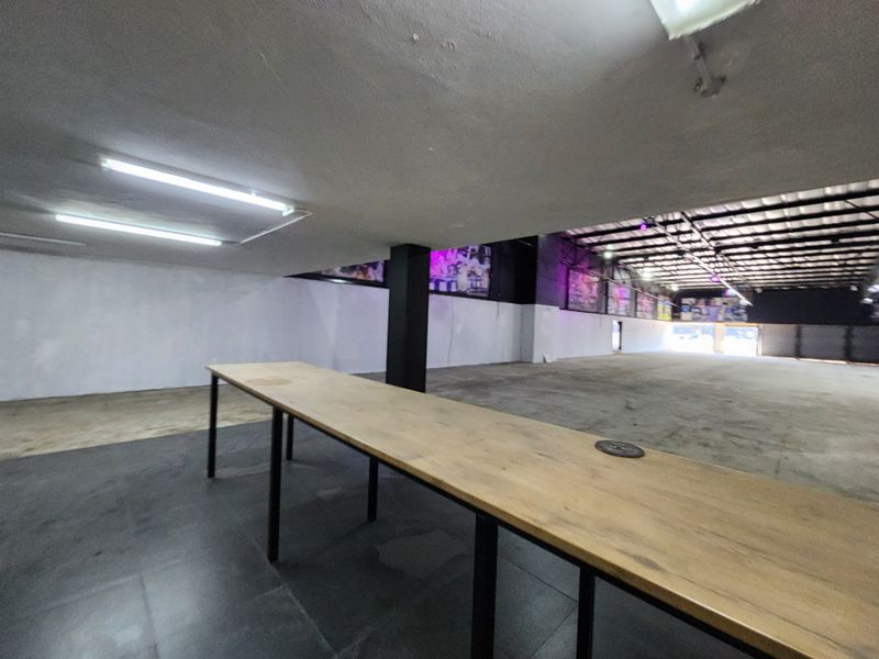 A large, open-plan retail or industrial space featuring exposed steel roof trusses, concrete flooring, and functional overhead fluorescent lighting.