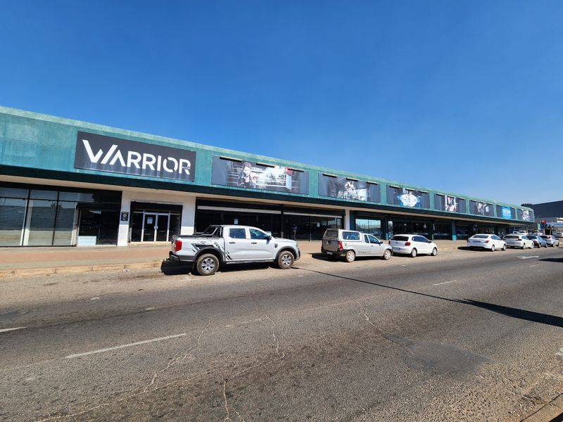 Front exterior view of a commercial retail strip center featuring large glass storefronts and prominent signage along the main road.