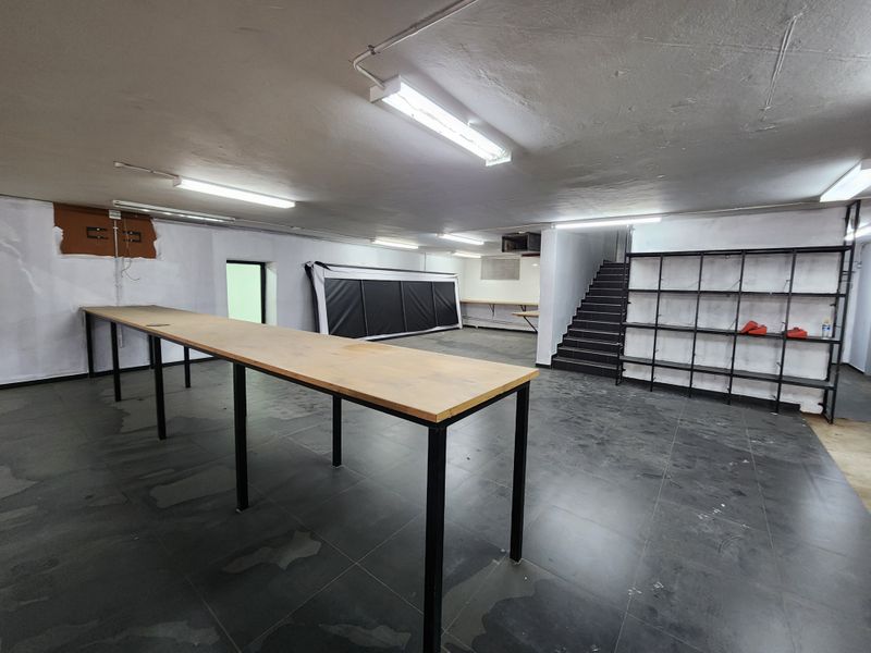 An open-plan utility or storage space featuring tiled flooring, built-in work counters, metal shelving, and a staircase leading to another level.