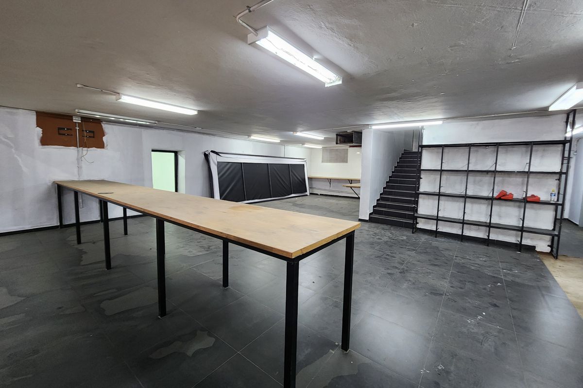 An open-plan utility or storage space featuring tiled flooring, built-in work counters, metal shelving, and a staircase leading to another level.