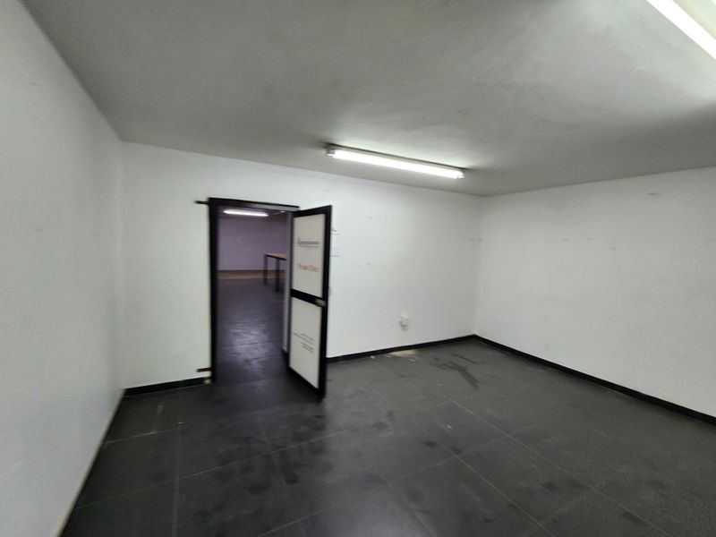 An empty, utilitarian commercial space featuring tiled flooring and fluorescent lighting, suitable for office or retail use.