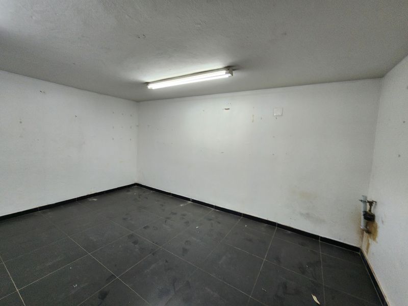 An empty utility space featuring tiled flooring, a fluorescent light fixture, and a wall-mounted plumbing connection, suitable for storage or functional use.