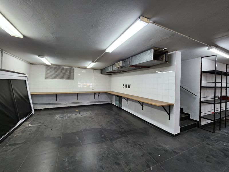 A functional utility or prep space featuring tiled walls, durable floor tiling, fixed wooden workbenches, and exposed ventilation ducting with direct staircase access.
