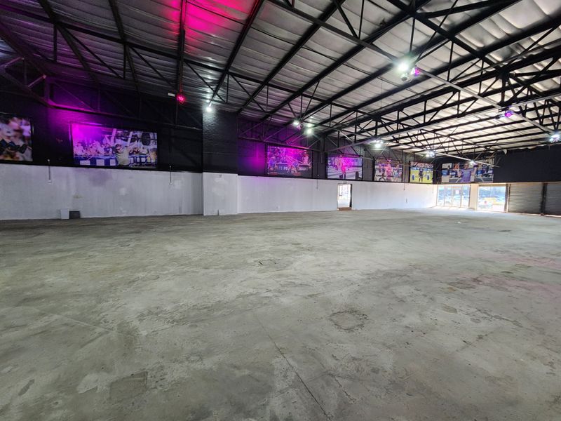 Expansive open-plan retail or industrial space featuring high exposed steel roof trusses, concrete flooring, and industrial lighting, suitable for various commercial applications.