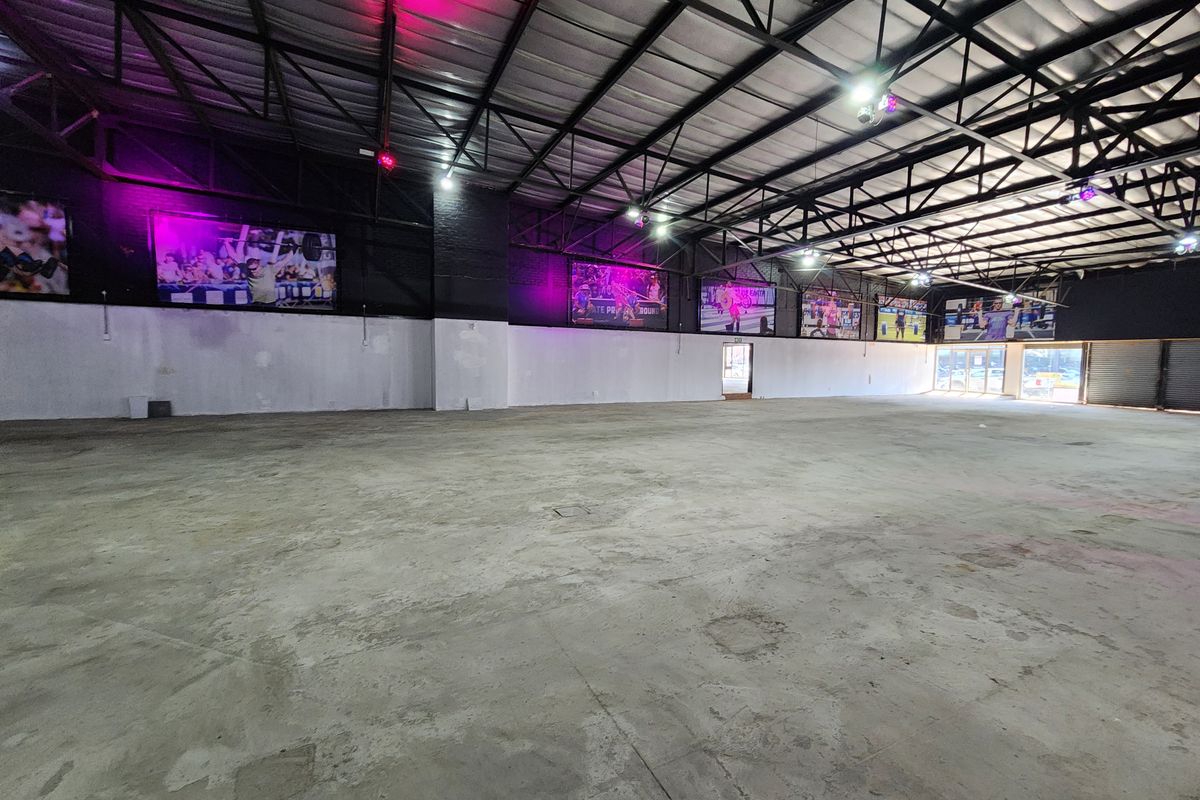 Expansive open-plan retail or industrial space featuring high exposed steel roof trusses, concrete flooring, and industrial lighting, suitable for various commercial applications.