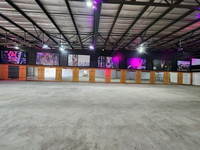 Spacious industrial-style gym area featuring exposed steel roof trusses, concrete flooring, and a long wall of mirrors, suitable for fitness or studio use.