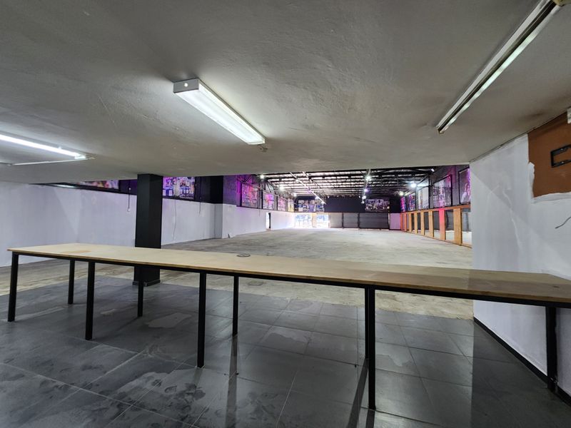 A large, open-plan retail or commercial space featuring a mix of tiled and concrete flooring, structural columns, and a mirrored wall section.