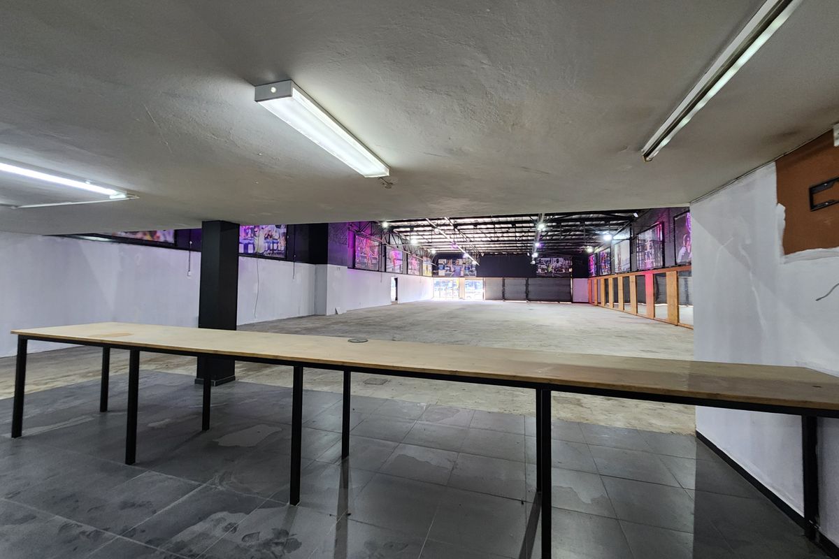A large, open-plan retail or commercial space featuring a mix of tiled and concrete flooring, structural columns, and a mirrored wall section.