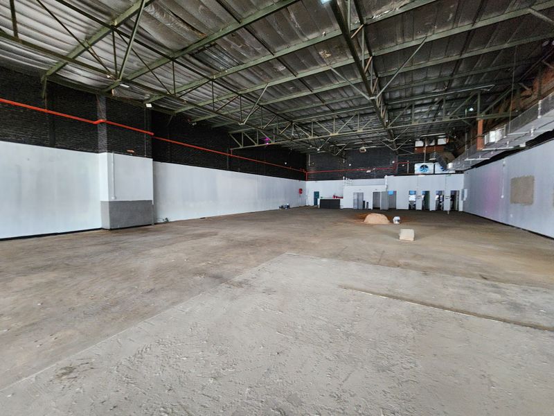 A large, open-plan industrial utility space featuring exposed steel roof trusses, concrete flooring, and exposed infrastructure, suitable for various commercial or retail applications.