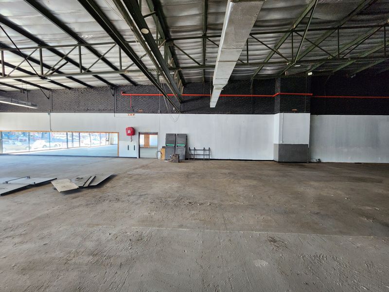 Spacious open-plan retail area featuring exposed steel roof trusses, industrial ducting, concrete flooring, and large display windows.
