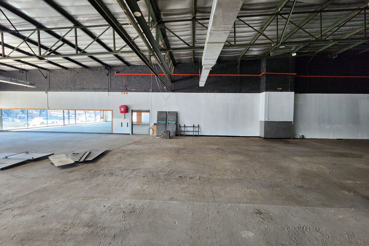 Spacious open-plan retail area featuring exposed steel roof trusses, industrial ducting, concrete flooring, and large display windows.