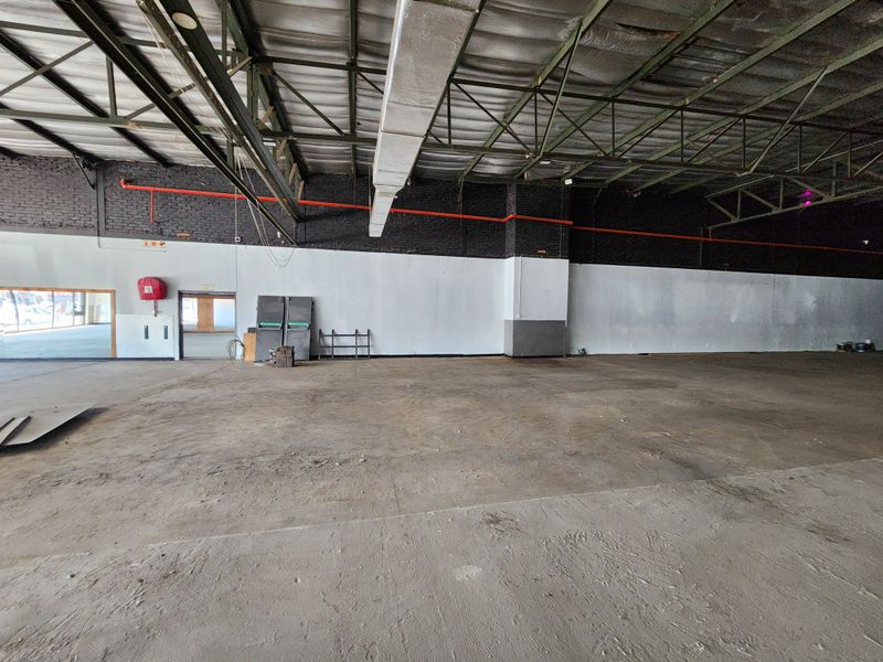 Large open-plan industrial retail space featuring exposed steel roof trusses, concrete flooring, and visible fire safety infrastructure.