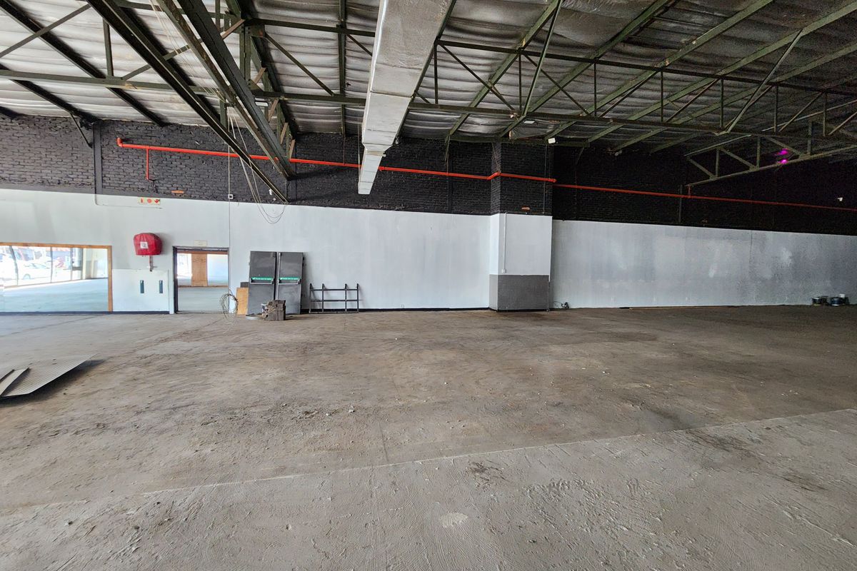 Large open-plan industrial retail space featuring exposed steel roof trusses, concrete flooring, and visible fire safety infrastructure.