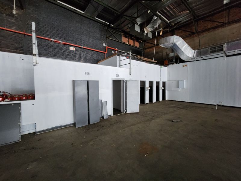 An expansive, industrial-style utility space featuring exposed brickwork, high ceilings with ducting, and multiple access points, suitable for warehouse or commercial workshop use.