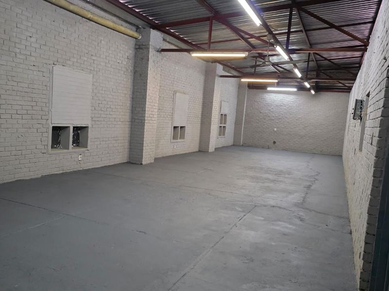 Spacious industrial utility area featuring exposed steel roof trusses, painted brick walls, and durable concrete flooring with integrated strip lighting.