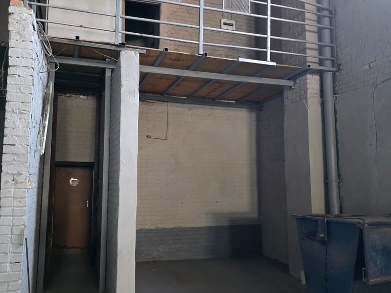 Industrial utility space featuring a mezzanine level with metal railing, exposed brick walls, and concrete flooring, suitable for storage or workshop use.
